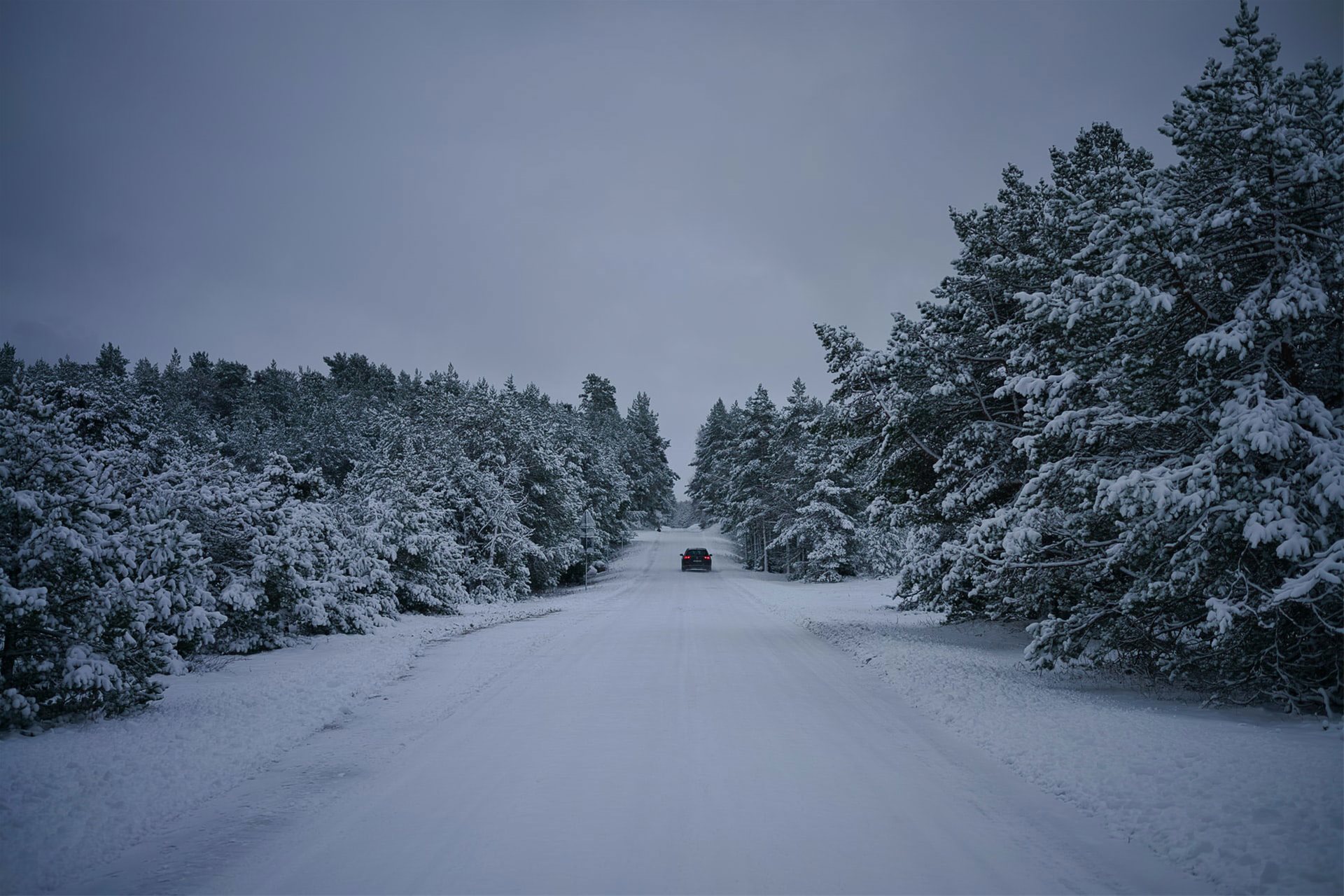 Bil kjører opp landevei dekket med snø
